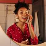 curly-woman-looks-in-mirror-and-puts-cream-under-h-2023-11-27-05-06-09-utc