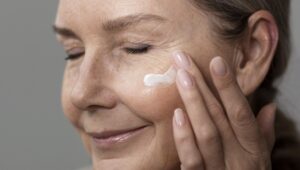 Side view old woman applying face cream